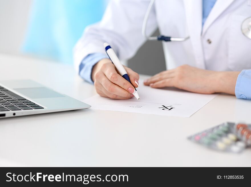 Female doctor filling up prescription form while sitting at the desk in hospital closeup. Physician finishing u