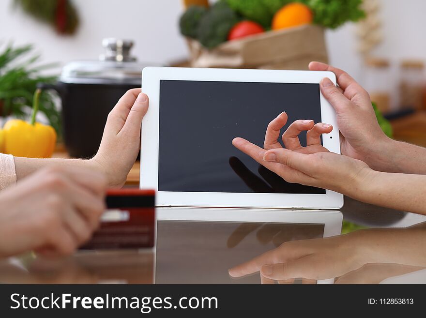 Closeup of human hands cooking in kitchen. Women discuss a menu using tablet computer. Copy space area at touch pad. Healthy meal, vegetarian food and lifestyle concepts.