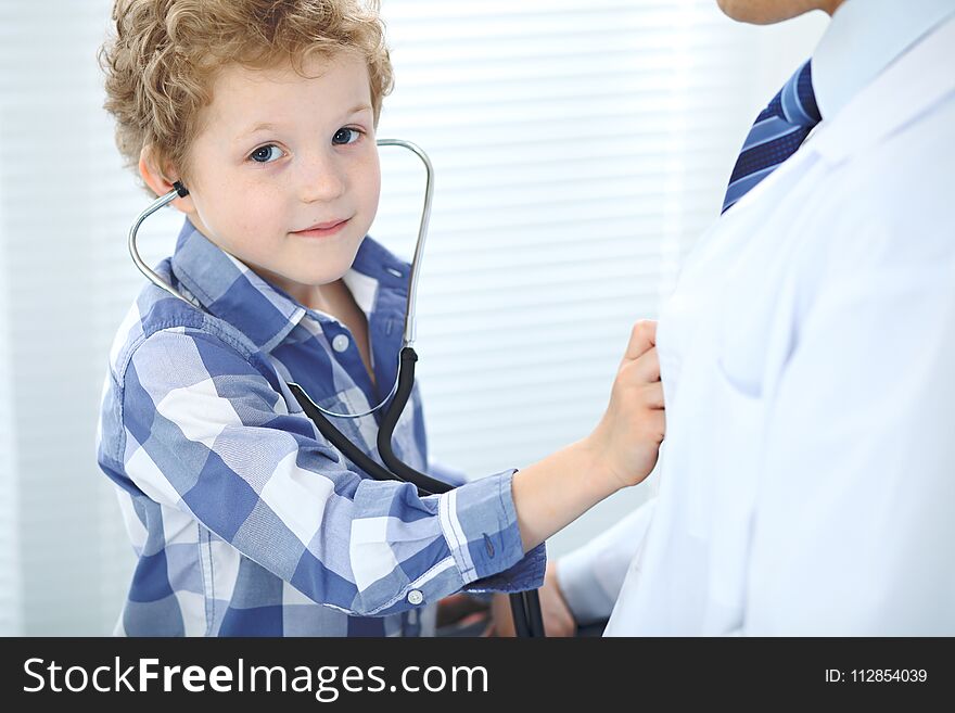 Doctor and child patient. Little boy play with stethoscope while physician communicate with him. Children`s therapy and trusting relationship in medicine concept.