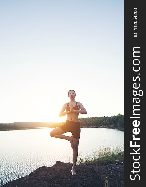 Young healthy woman is practicing yoga at mountain lake during sunset.