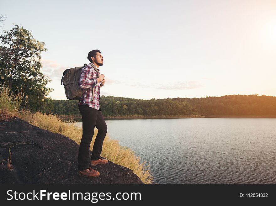 Hipster hiker man standing on the rock and enjoying sunset over