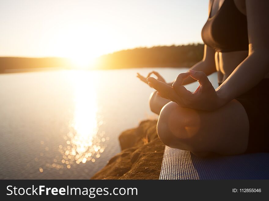 Young healthy woman is practicing yoga at mountain lake during sunset.