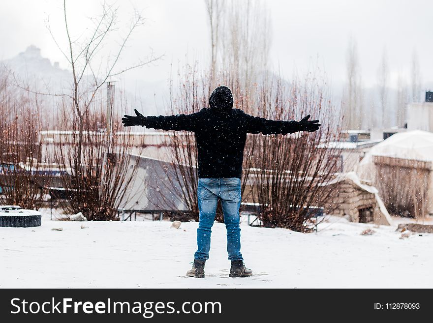 Person Wears Black Jacket and Blue Denim Jeans Standing on Snow Covered Field