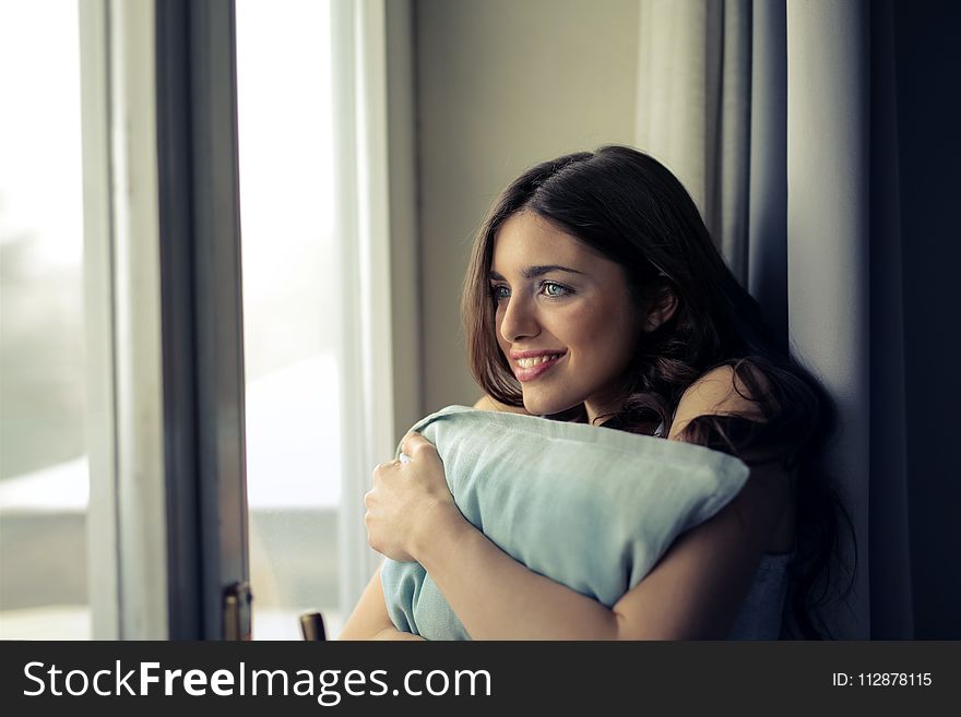 Woman Hugging White Pillow Beside Glass Door