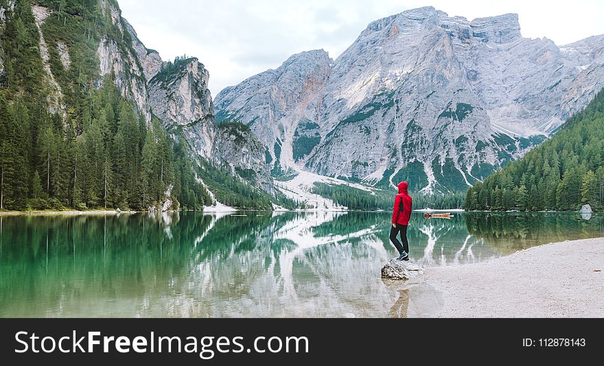 Man Wearing Red Hoodie Standing Near Body of Water With View of Mountains