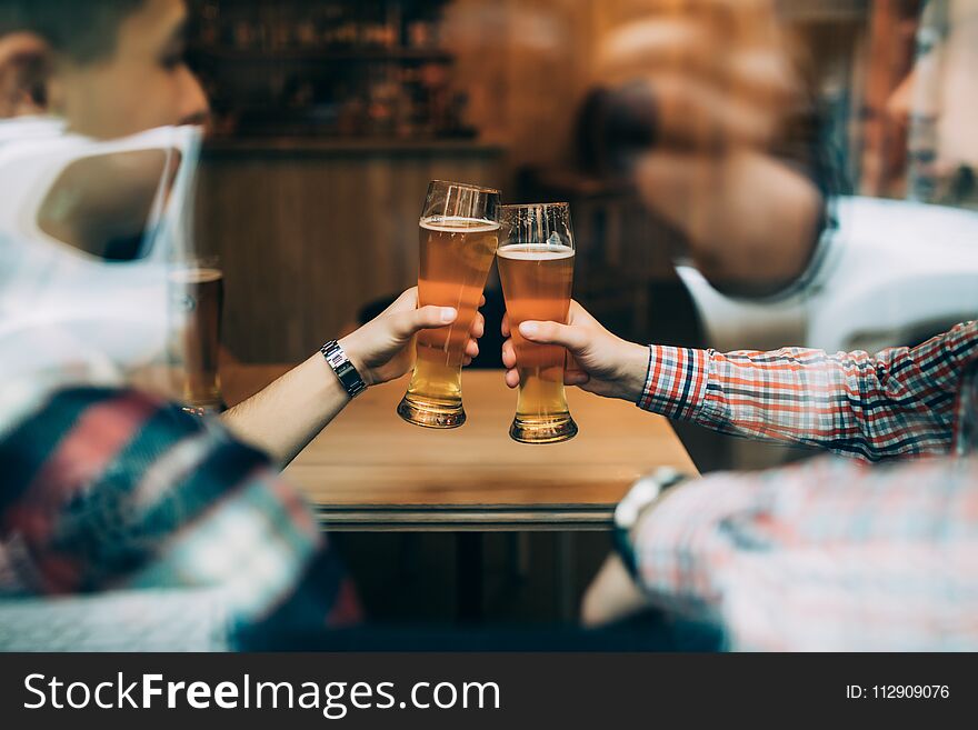 Close up hands of friends sitting at the pub cheers with beers glasses trough window.