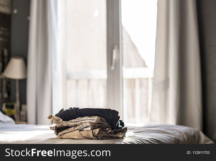 Pile of clothes on bed beside windows