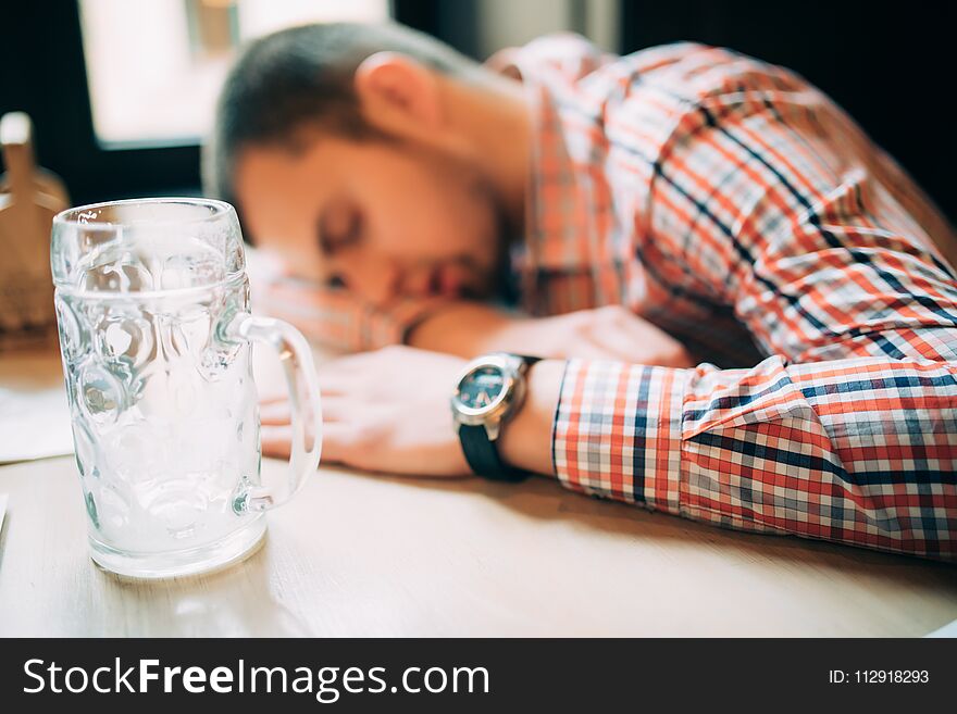 Drunk again. Drunk male customer leaning at the bar counter and sleeping while glass with beer standing near him