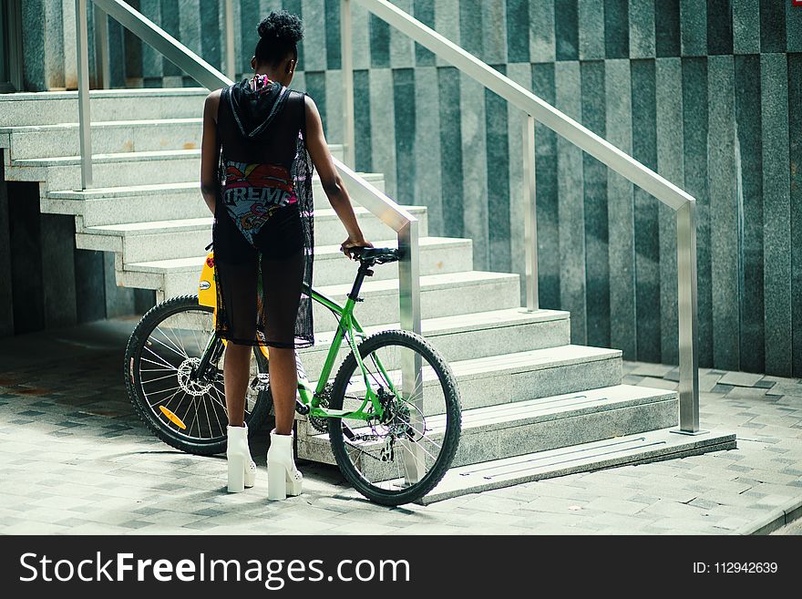 Man in Black Sleeveless Shirt Holding Green Mountain Bike Near Metal Staircase
