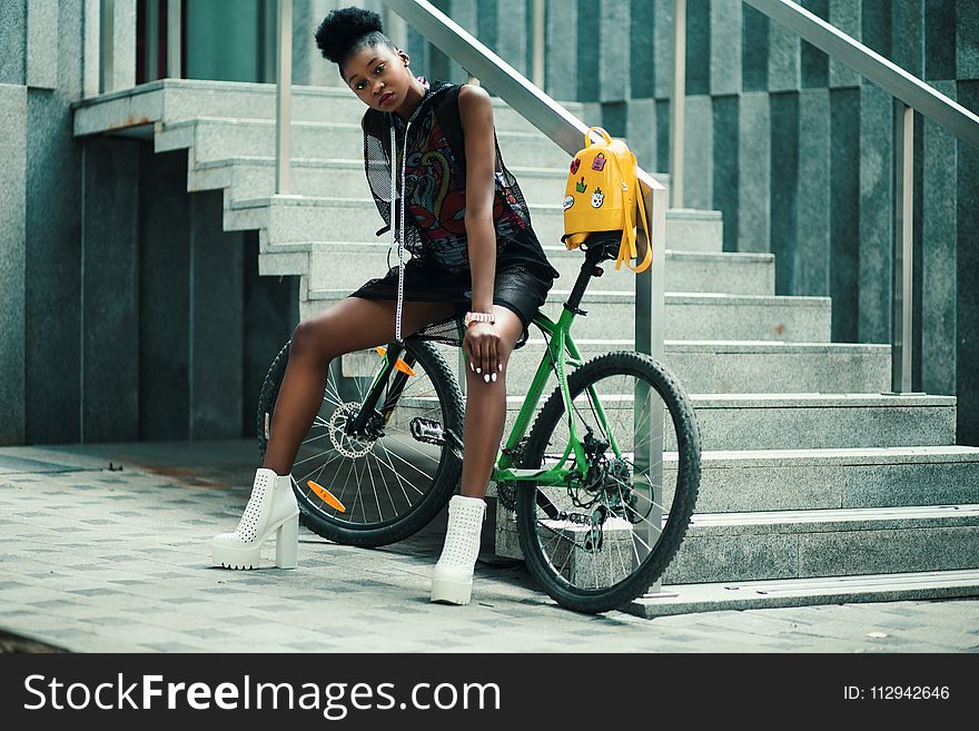 Woman in Black Sleeveless Dress Sitting on Green Bike