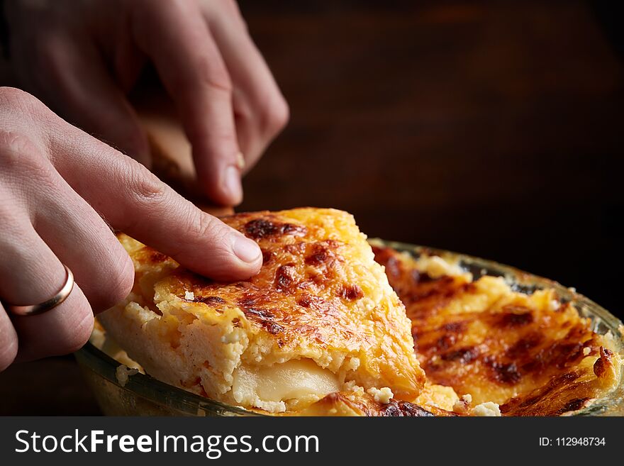 A piece of lasagna cooked in a glass pan over vintage wooden background, top view, close-up, selective focus