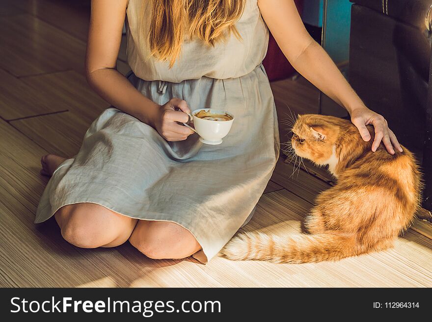 Young woman is drinking coffee and stroking the cat.