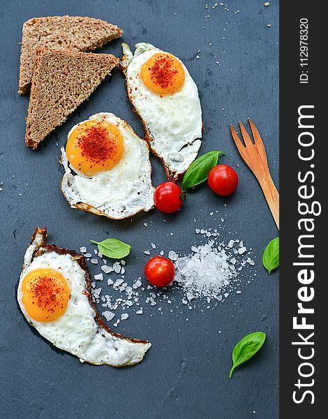 Bio Fresh fried eggs ,salt, fresh basil, cherry tomatoes and bread on black background .