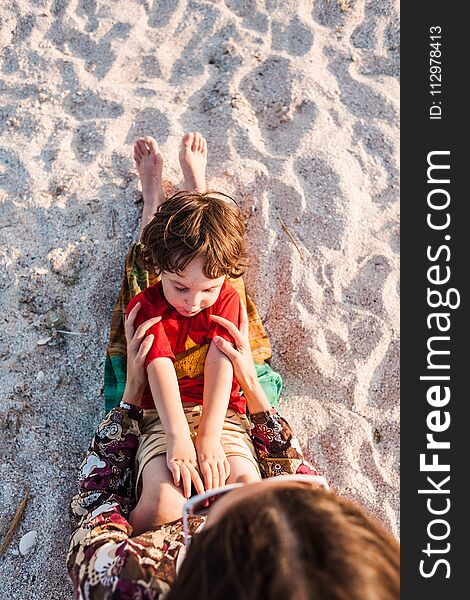 Child with mom on the beach. The boy is playing with his mother. The kid lies on the sand. A women is resting with her son at the seaside.