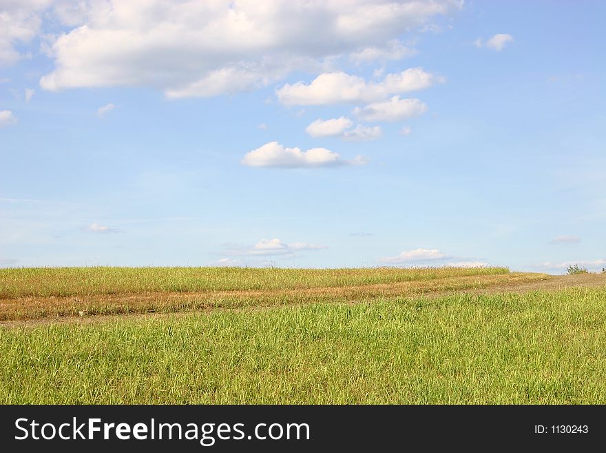 A road through green field of grass reaches the sky of blue. A road through green field of grass reaches the sky of blue