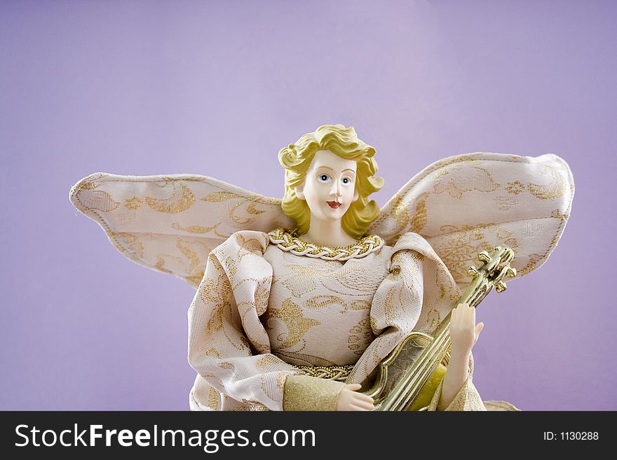 A lovely porcelain Christmas angel with blond hair and blue eyes in gold brocade holds a mandolin.