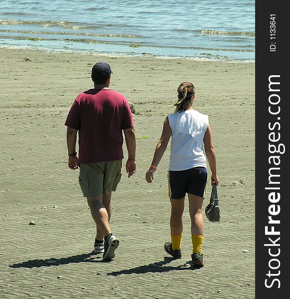 A father and daughter walking on the beach during a break in a fastball tournament. A father and daughter walking on the beach during a break in a fastball tournament