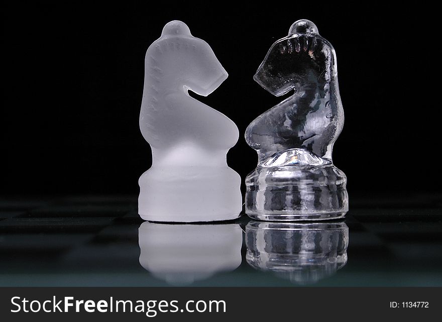 Opposing knights from a glass chess set face off.