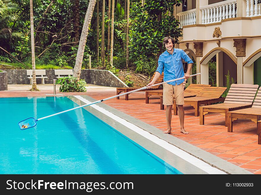 Cleaner of the swimming pool . Man in a blue shirt with cleaning equipment for swimming pools, sunny.