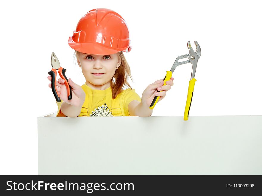 A nice little girl in a construction helmet and a yellow T-shirt peeped out from behind a white advertising banner.Girl in a construction helmet peeks out from behind a billboard.