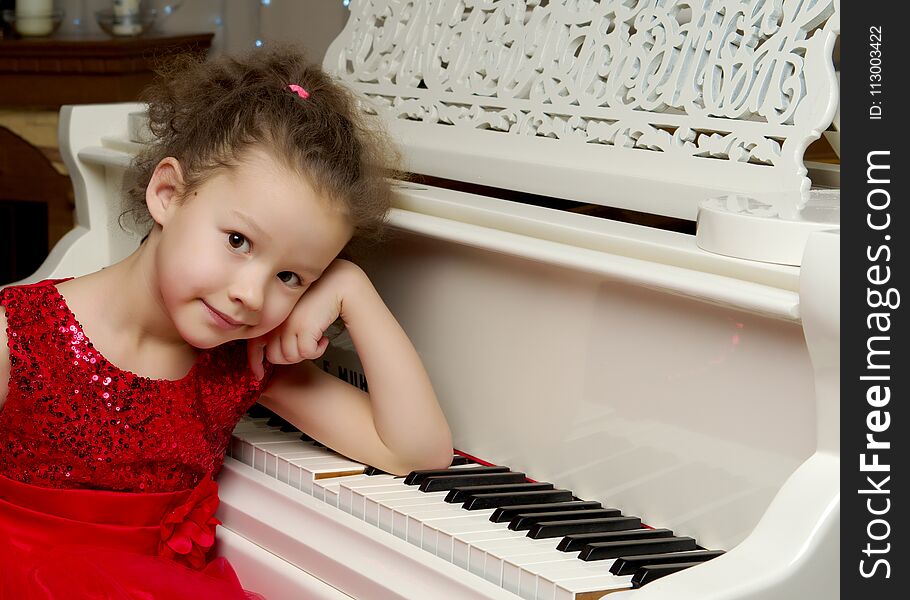 A nice little girl is playing on a big white piano. The concept of musical and aesthetic education of a child. A nice little girl is playing on a big white piano. The concept of musical and aesthetic education of a child.