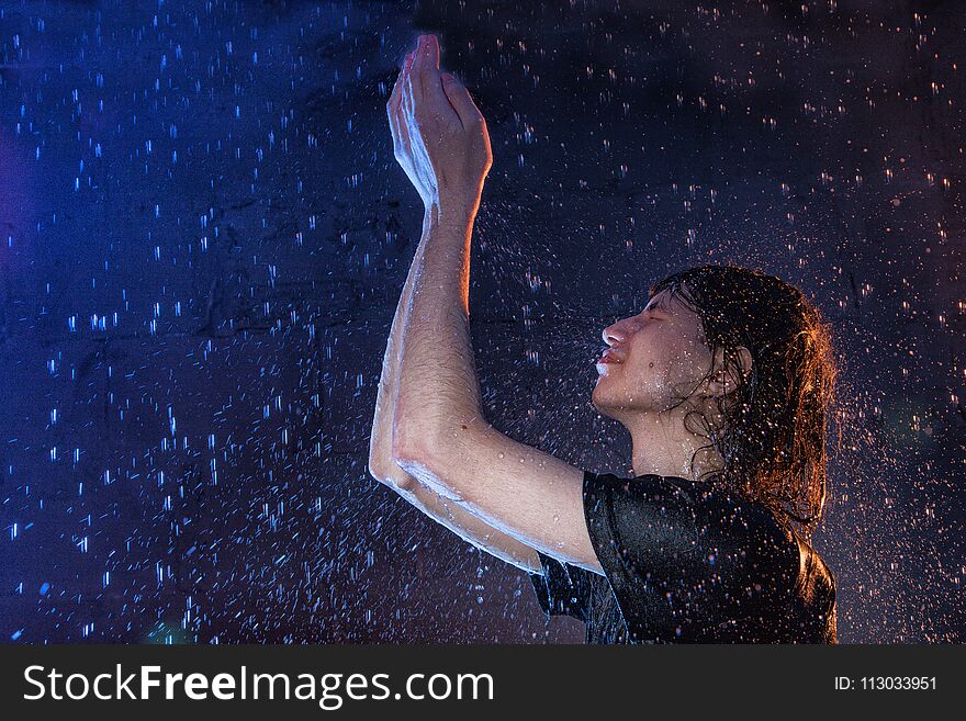 Attractive young man in black wet clothes under the rain and splash of water during studio photo shoot
