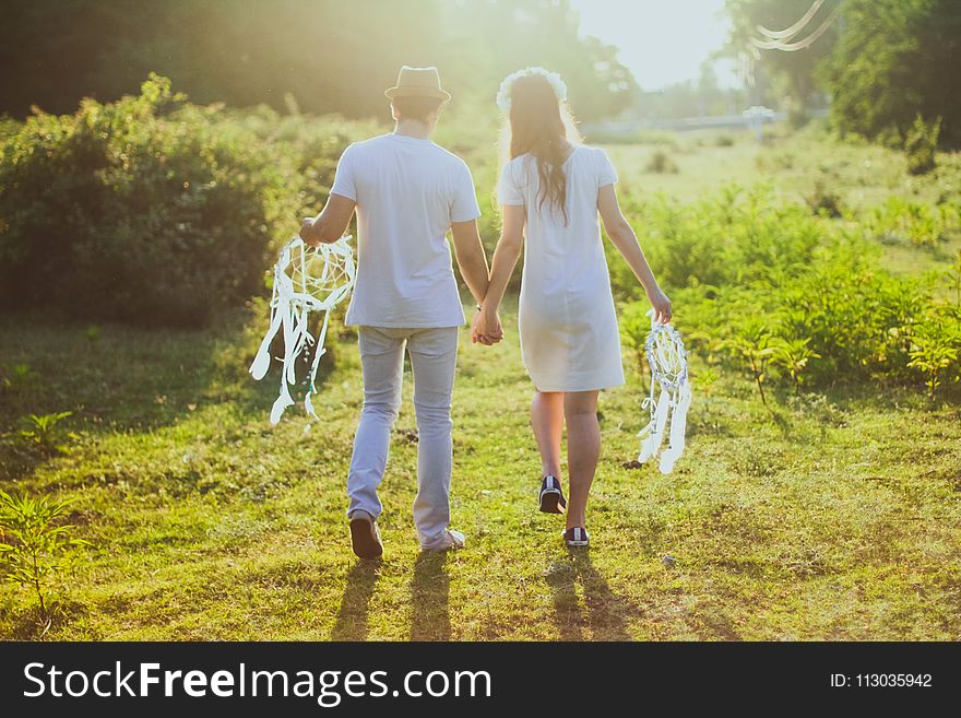 Coupe With White Dress and Suit Holding a White Dreamcatcher While Walking on Green Grass