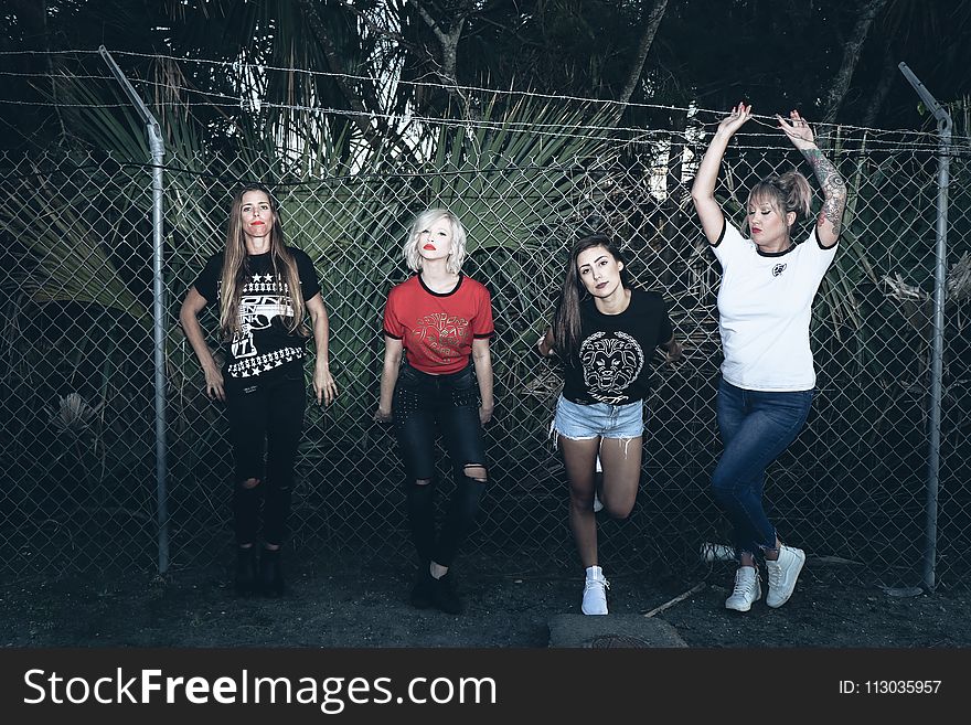 Four Women Leaning on Gray Steel Fence