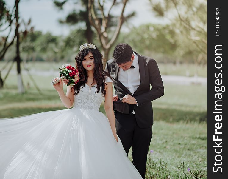 Woman in Wedding Dress Holding Flower With Man in Black Blazer