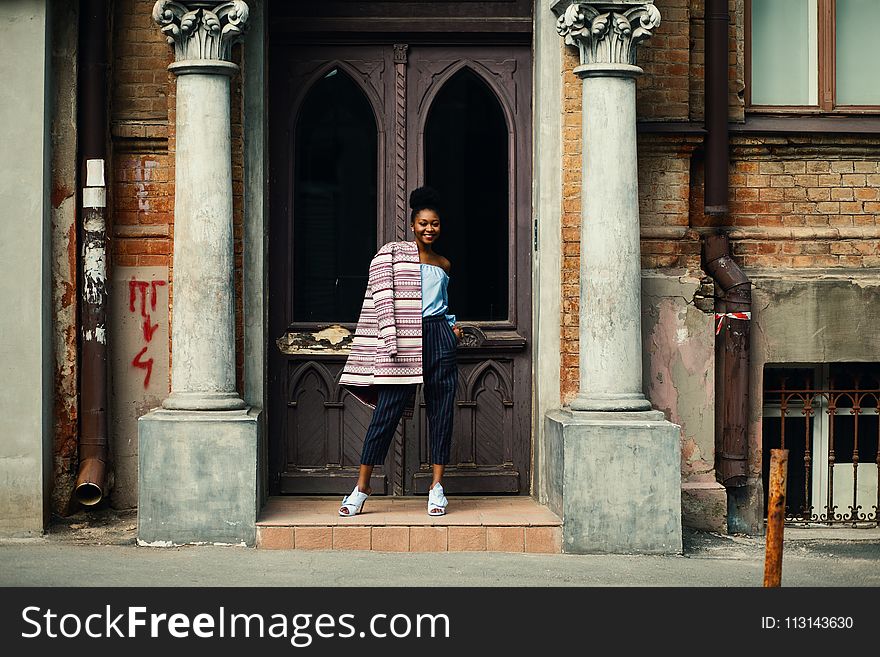 Woman In Blue Strapless Top And Black Pants Standing Next To Brown Wooden Door