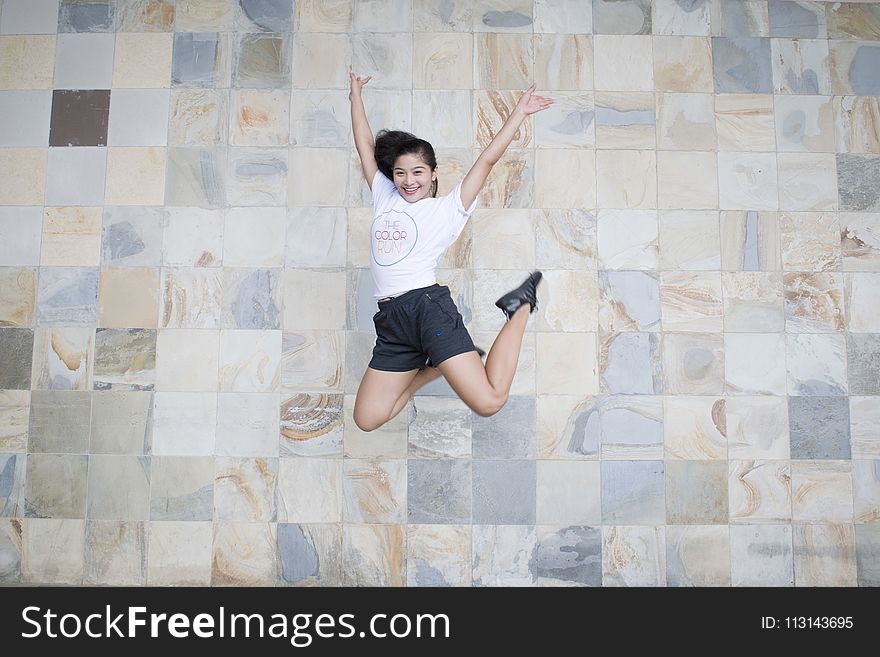 Woman in White Shirt and Black Shorts Taking Jump Shot Near Wall