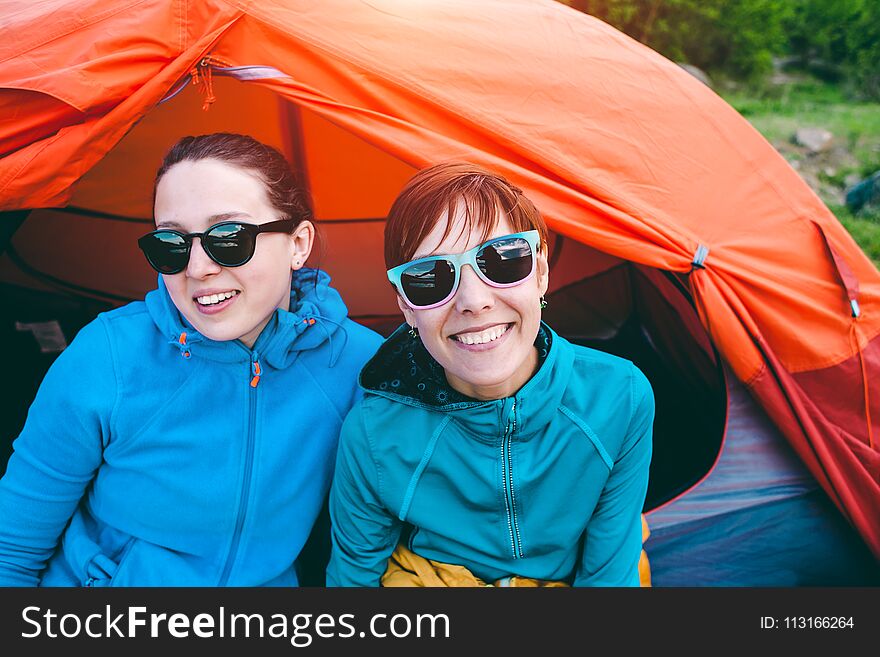 Two girls are sitting in a tent. Girlfriends communicate in nature. Women in sleeping bags. Friends in the campsite. Smiling brunettes talking. Two girls are sitting in a tent. Girlfriends communicate in nature. Women in sleeping bags. Friends in the campsite. Smiling brunettes talking.