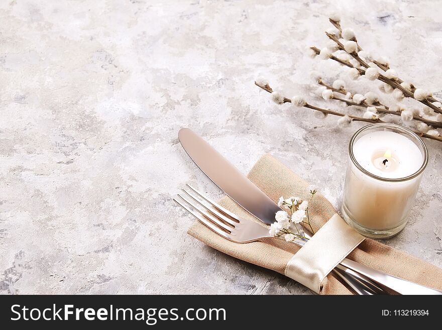 Easter table setting composition: fork, knife candle, wildflowers, willow on plate w/ napkin, white stucco plaster texture background. Close up, top view, copy space. Easter table setting composition: fork, knife candle, wildflowers, willow on plate w/ napkin, white stucco plaster texture background. Close up, top view, copy space