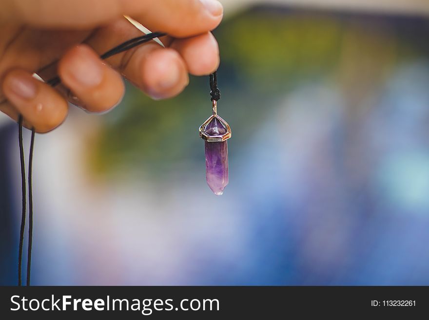 Person Holding Black Necklace With Purple Stone Pendant