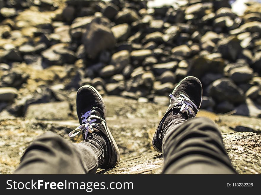 Shallow Focus Photography of Person Wearing Gray Jeans Sitting in Front Rocks