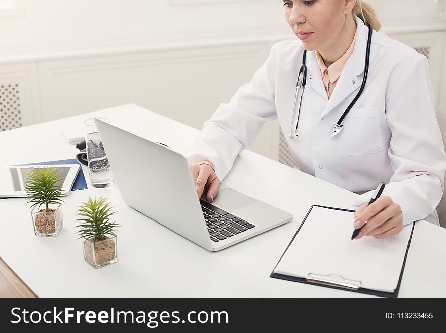 Female doctor using laptop and writing notes while working at her office. Always ready to help, medicine concept, copy space. Female doctor using laptop and writing notes while working at her office. Always ready to help, medicine concept, copy space