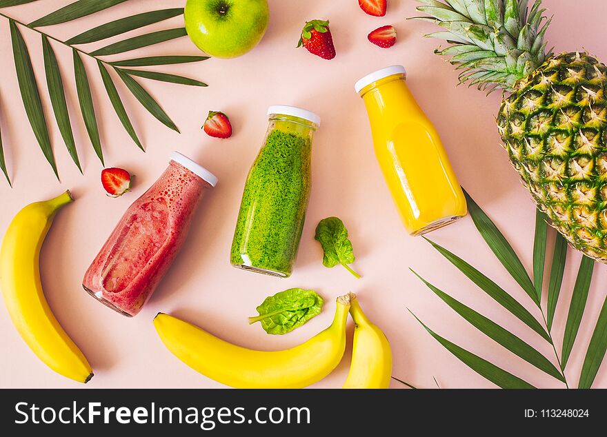 Flat-lay of colorful smoothies in bottles with fresh fruits.