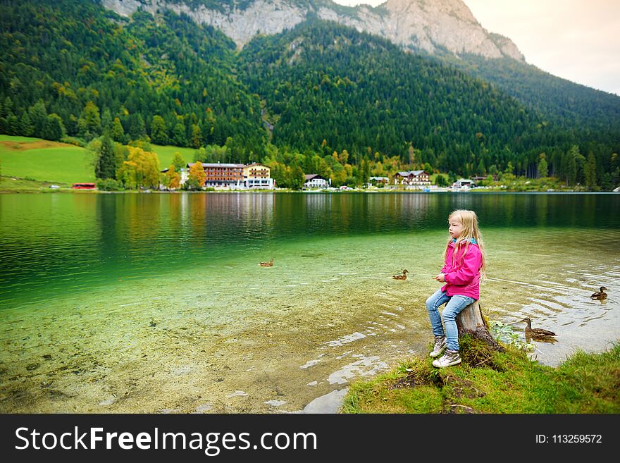 Cute little girl enjoying the view of wonderful green waters of Hintersee lake. Amazing autumn landscape of Bavarian Alps on the A