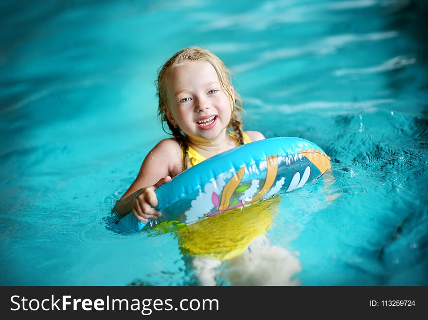 Cute little girl playing with inflatable ring in indoor pool. Child learning to swim. Kid having fun with water toys.