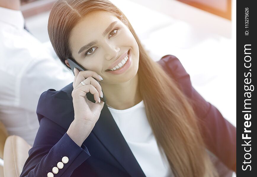 Smiling female employee talking on a mobile with a client sitting behind a Desk