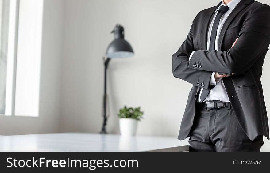 Businessman standing in office with crossed arms, close up view of his body.