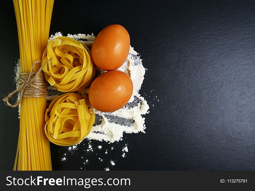 Different kinds of pasta tagliatelle, spaghetti, italian foods concept and menu design, raw eggs and flour on a shale board, empty space for text, top view, set.