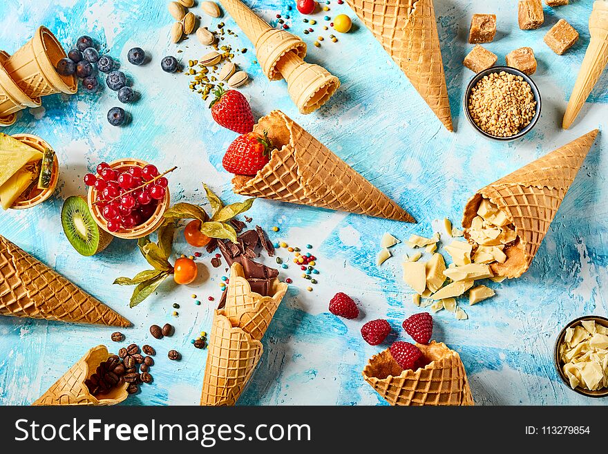 Crispy wafer cones filled with fruits and sweet ingredients against blue background. Crispy wafer cones filled with fruits and sweet ingredients against blue background