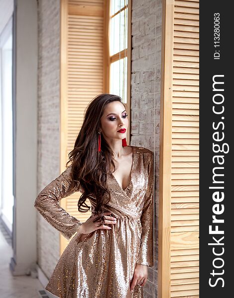 Amazing luxury woman in stylish gold shining party dress . Bright smokey eyes make up, red full lips, healthy wavy hairs
