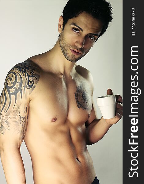 Tattooed Man With Bare Torso Is Holding A Cup
