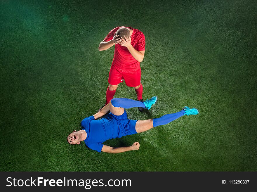 Male soccer player suffering from leg injury on football green field at stadium. The professional football, soccer player and human emotions concept. The players on green grass of football field background
