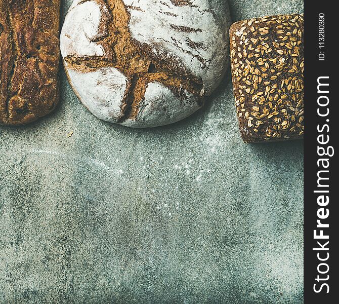 Various bread selection flat-lay. Top view of Rye, wheat and multigrain rustic bread loaves over grey background, copy space, square crop. Various bread selection flat-lay. Top view of Rye, wheat and multigrain rustic bread loaves over grey background, copy space, square crop
