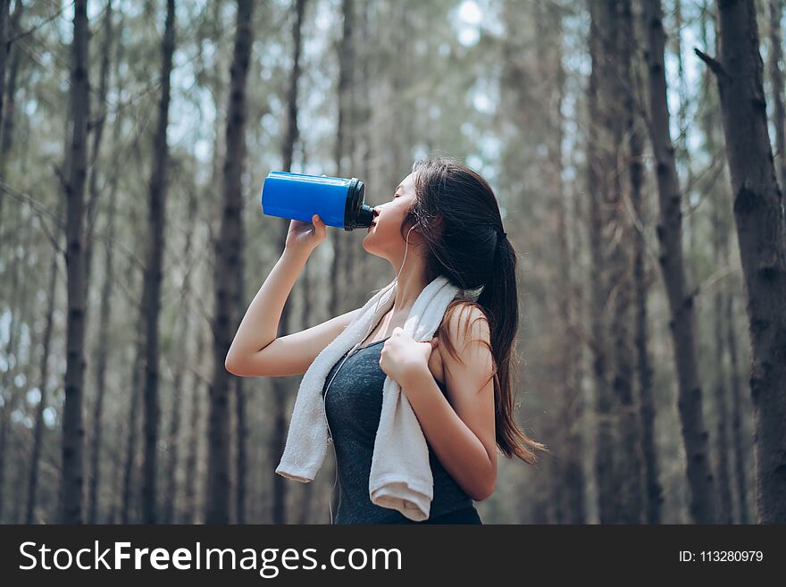 Beautiful asian woman drinking protein shake in the forest nature autumn for relaxing recovery healthy lifestyle with listening music with earphone sport outdoor.