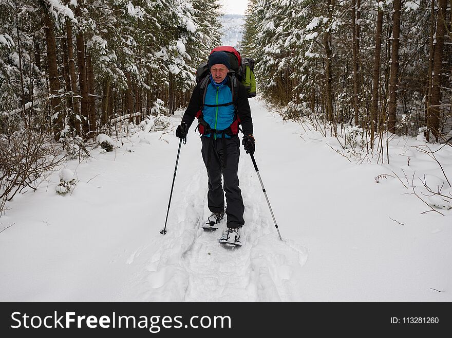 Hiker, with big backpack, is walking in snowshoes