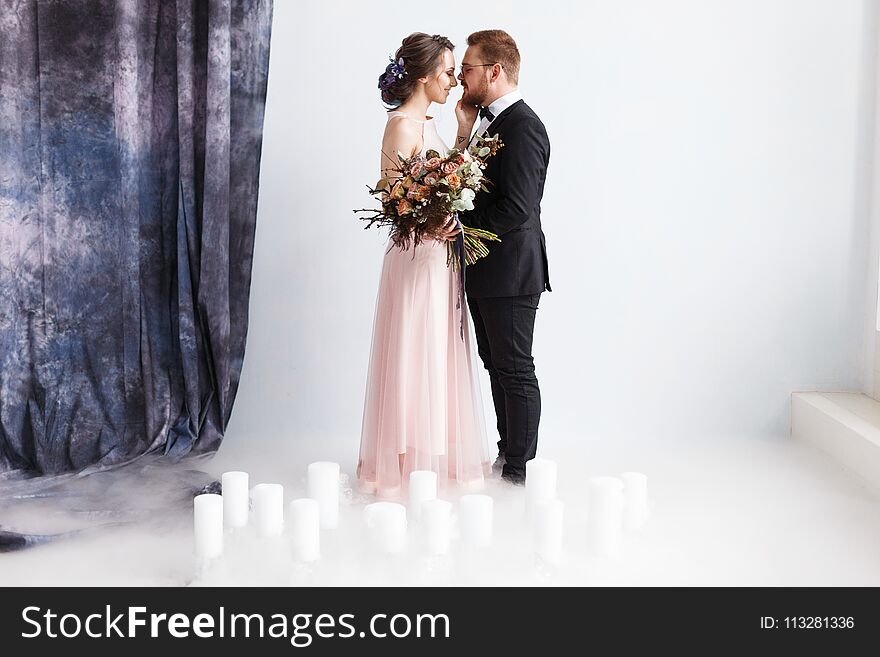 Full-length portrait of pretty newlyweds with bouquet. isolated white background. Studio horizontal shot with dry ice smoke.